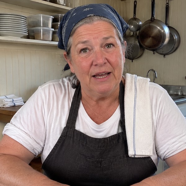 Lorraine Marino in her kitchen, in a navy bandana and a dark apron, a side towel over her shoulder